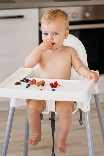Vista frontal lindo bebé en trona eligiendo qué fruta comer