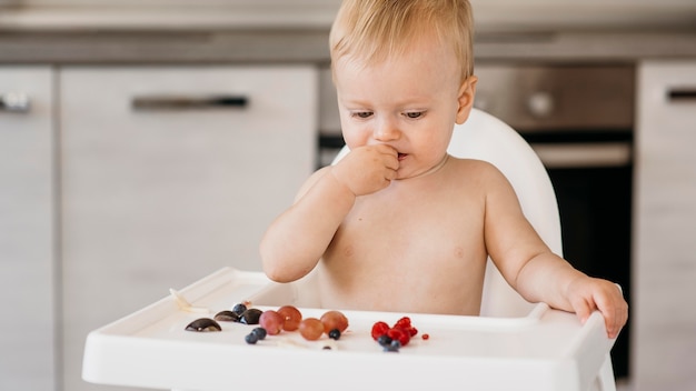 Vista frontal lindo bebé en trona eligiendo qué frutas comer
