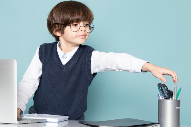 Una vista frontal lindo chico de negocios en jamper clásico azul posando delante de la computadora portátil de plata trabajando moda de trabajo empresarial