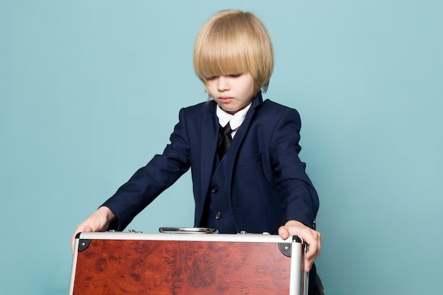 Foto gratuita una vista frontal lindo chico de negocios en traje clásico azul posando sosteniendo maleta marrón-plateada moda de trabajo comercial