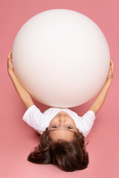 Una vista frontal lindo niño adorable en camiseta blanca jugando con bola blanca redonda en el espacio rosa