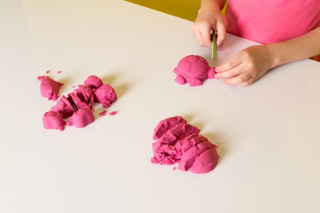 Una vista frontal lindo niño adorable en camiseta rosa jugando con arena cinética colorida