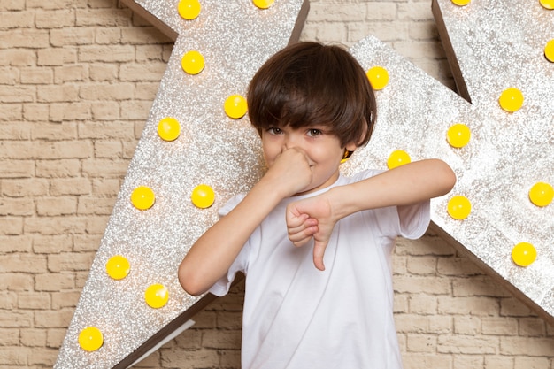 Foto gratuita una vista frontal lindo niño pequeño en camiseta blanca jeans oscuros en la estrella diseñada soporte amarillo y fondo claro