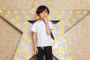 Foto gratuita una vista frontal lindo niño pequeño en camiseta blanca jeans oscuros en la estrella diseñada soporte amarillo y fondo claro