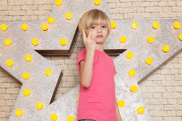 Foto gratuita una vista frontal lindo niño pequeño en camiseta rosa jeans grises en la estrella diseñada soporte amarillo y fondo claro