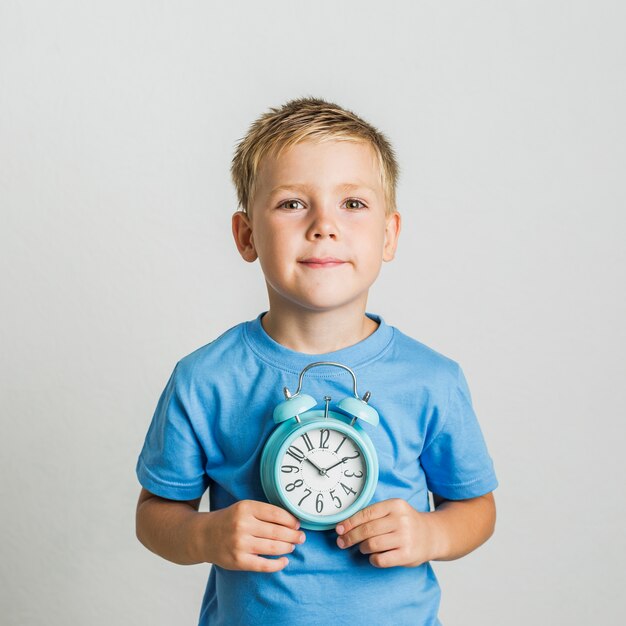 Vista frontal lindo niño sosteniendo un reloj