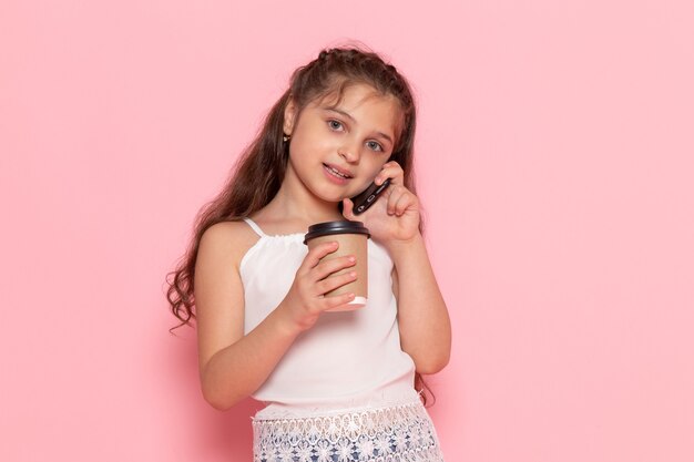 Una vista frontal lindo niño sosteniendo una taza de café y hablando por teléfono