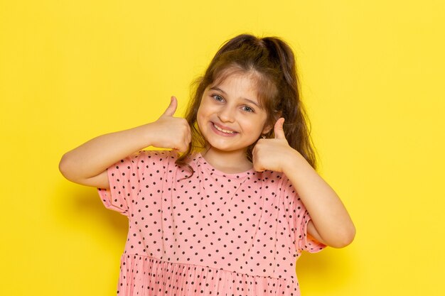 Una vista frontal lindo niño en vestido rosa sonriendo y mostrando como signo