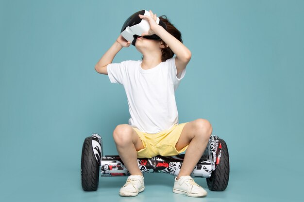 Una vista frontal little boy sonriente jugando vr en segway en el piso azul