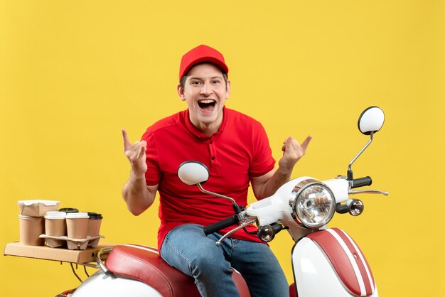 Vista frontal del loco joven emocional con blusa roja y sombrero entregando pedidos sobre fondo amarillo