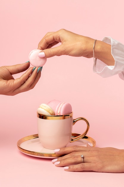 Vista frontal de macarons en copa de oro para el día de san valentín con manos de mujeres