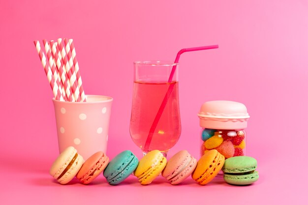 Foto gratuita una vista frontal de macarons franceses con bebida fresca, caramelos de colores y caramelos de palo en rosa, pastelería de galletas y pasteles