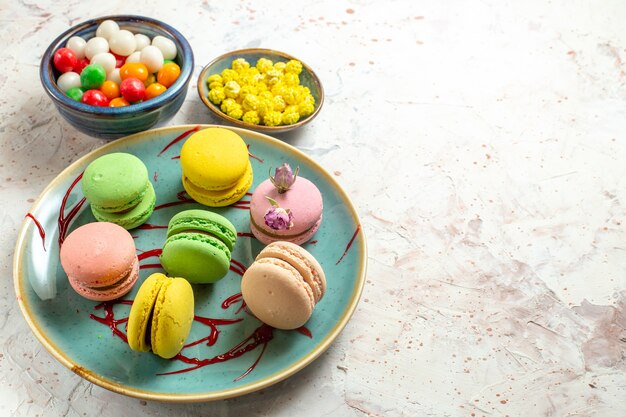 Vista frontal de macarons franceses con caramelos en la galleta de la galleta de la torta del color de la tabla blanca