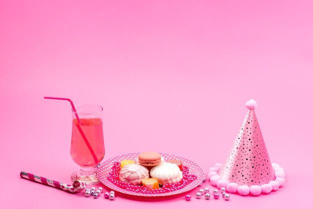 Una vista frontal de macarons franceses dentro de la placa junto con la bebida y la gorra de cumpleaños en rosa, celebración de regalos de fiesta