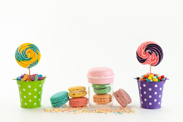 Una vista frontal de macarons franceses junto con caramelos de colores dentro de cestas en blanco, paleta dulce de azúcar de color