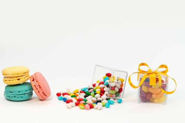 Una vista frontal de macarons franceses junto con caramelos de colores sobre blanco, color pastel de galleta