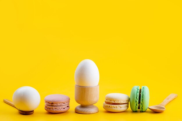 Una vista frontal de macarons franceses junto con huevos duros en amarillo, pastel de galletas dulces de azúcar
