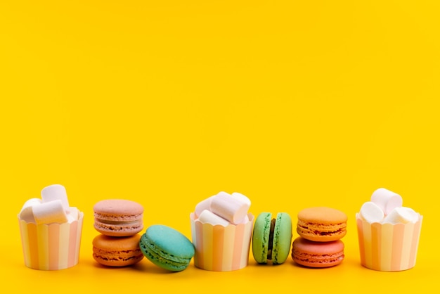 Una vista frontal de macarons franceses junto con malvaviscos blancos aislados en amarillo, confitería de dulces de tarta