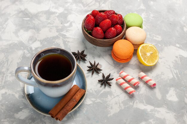 Vista frontal de macarons franceses con té, canela y fresas frescas sobre superficie blanca, fruta, baya, pastel, galleta, dulce