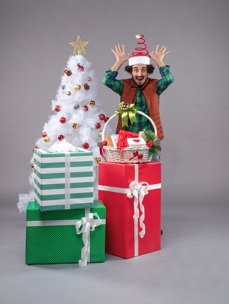 Vista frontal macho joven alrededor de regalos de vacaciones en piso ligero regalo de navidad humano año nuevo