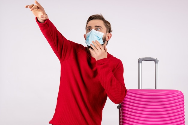Vista frontal macho joven con bolsa rosa en máscara apuntando a la pared blanca voyage covid- vuelo viaje vacaciones emoción virus