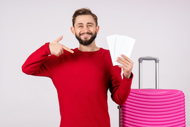 Vista frontal macho joven con bolsa rosa y sosteniendo billetes de avión en la pared blanca viaje vuelo viaje vacaciones emoción foto turista