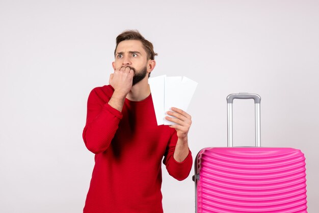 Vista frontal macho joven con bolsa rosa y sosteniendo boletos en la pared blanca viaje color viaje vacaciones turísticas foto emoción