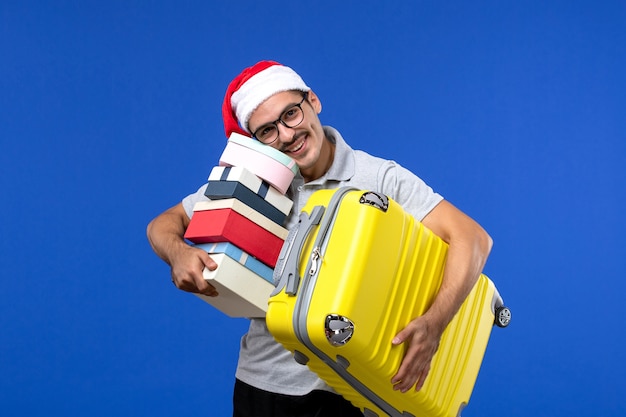 Vista frontal macho joven bolsa de transporte y regalos en aviones de vacaciones de vuelo de pared azul