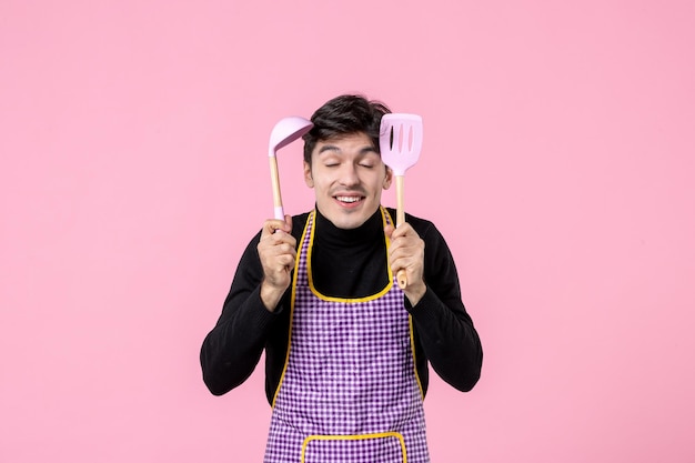 Vista frontal macho joven en cabo sosteniendo cucharas en rosa