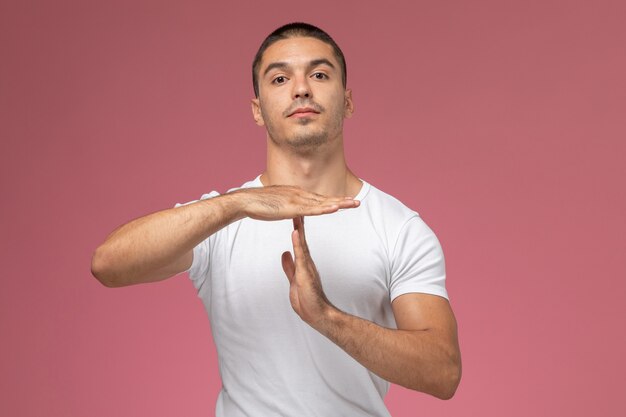 Vista frontal macho joven con camisa blanca mostrando signo de rotura sobre fondo rosa