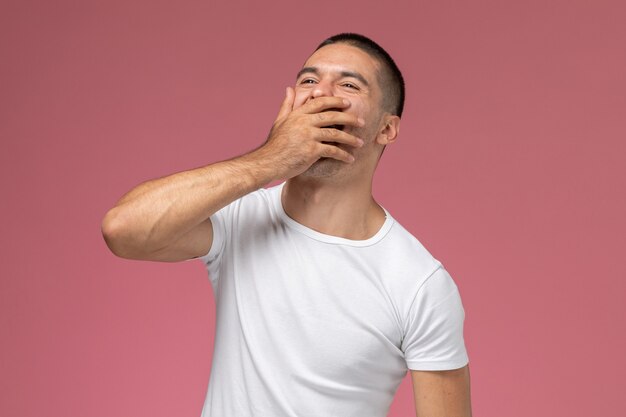 Vista frontal macho joven en camisa blanca riendo fuertemente sobre fondo rosa