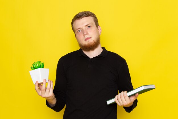 Vista frontal del macho joven en camisa negra con planta y cuaderno