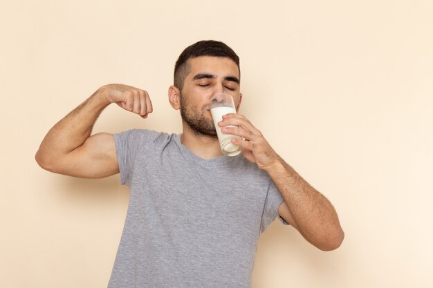 Vista frontal macho joven en camiseta gris bebiendo leche en beige ¡