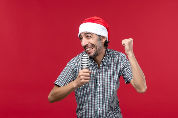 Vista frontal macho joven cantando con micrófono sobre fondo rojo.