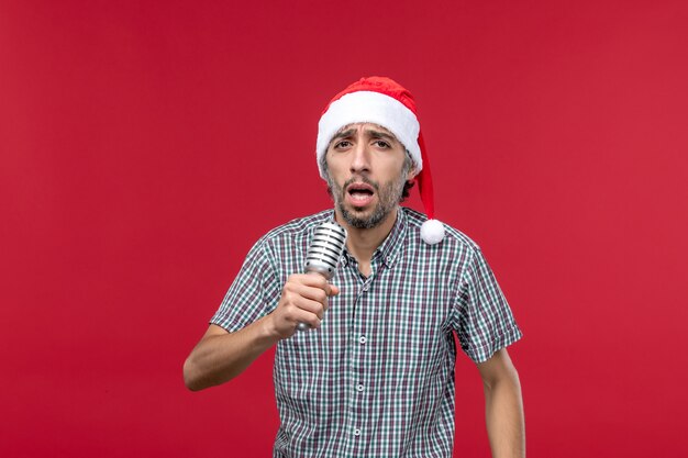 Vista frontal macho joven cantando con micrófono sobre fondo rojo.