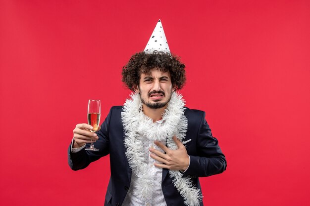 Vista frontal macho joven celebrando el año nuevo que viene en la pared roja fiesta de navidad