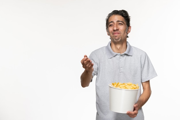 Vista frontal macho joven comiendo papas fritas riendo sobre superficie blanca