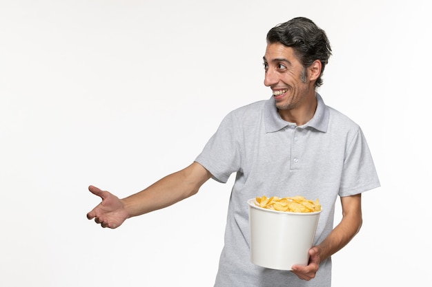 Vista frontal macho joven comiendo papas fritas riendo sobre superficie blanca