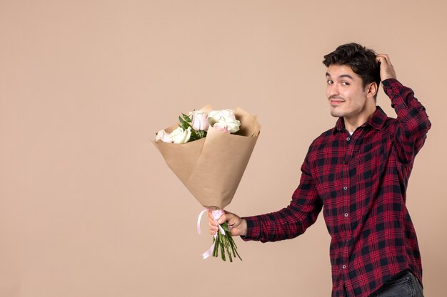 Vista frontal macho joven dando hermosas flores en la pared marrón