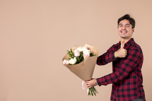 Foto gratuita vista frontal macho joven dando hermosas flores en la pared marrón