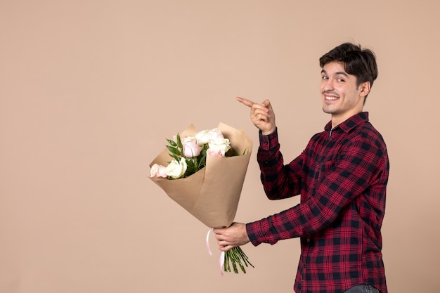 Vista frontal macho joven dando hermosas flores en la pared marrón