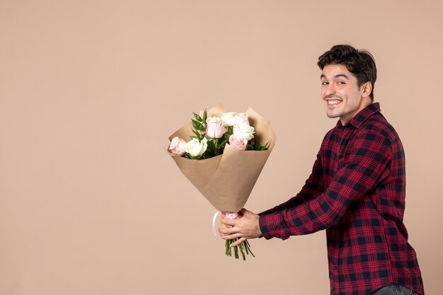 Vista frontal macho joven dando hermosas flores en la pared marrón