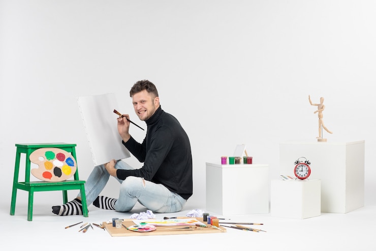 Foto gratuito vista frontal macho joven dibujo pintura con borla en blanco arte de pared colores pintura dibujo artista