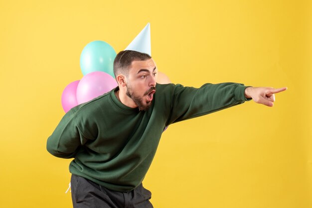 Vista frontal macho joven escondiendo globos de colores detrás de su espalda en amarillo