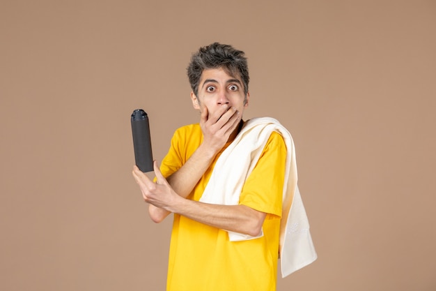 Vista frontal macho joven con espuma y toalla preparándose para afeitarse la cara sobre fondo de color rosa