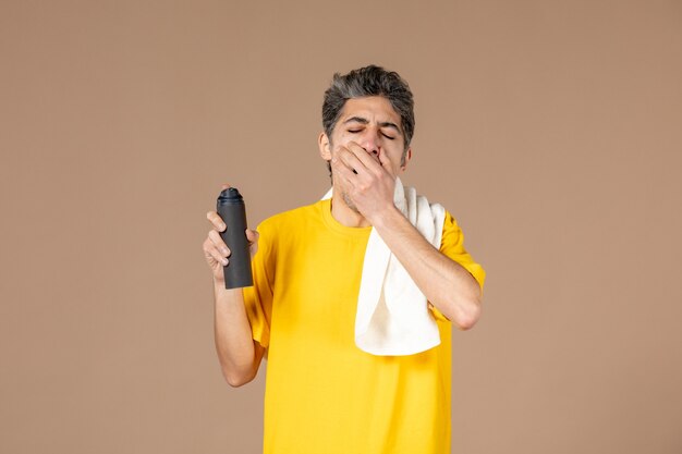 Vista frontal macho joven con espuma y toalla preparándose para afeitarse la cara sobre fondo de color rosa