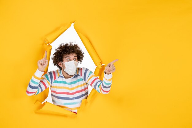 Vista frontal macho joven en máscara estéril en color amarillo rasgado covid- salud foto humana virus pandémico