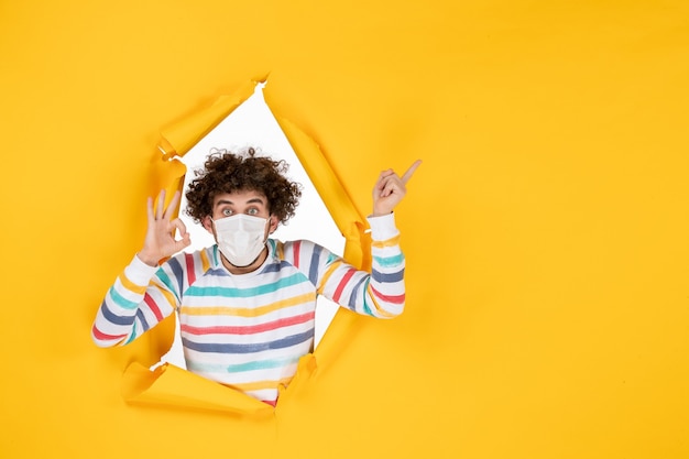 Vista frontal macho joven en máscara estéril en foto en color amarillo covid- virus de la pandemia de salud humana