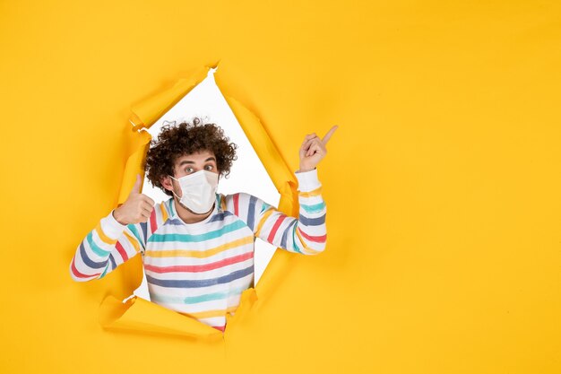 Vista frontal macho joven en máscara estéril en foto en color amarillo covid- virus de la pandemia de salud humana