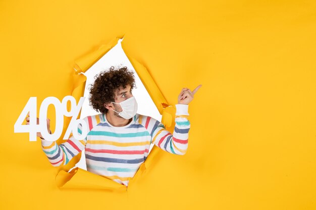 Vista frontal macho joven en máscara sosteniendo la escritura sobre el virus amarillo pandemia comercial salud covid venta color